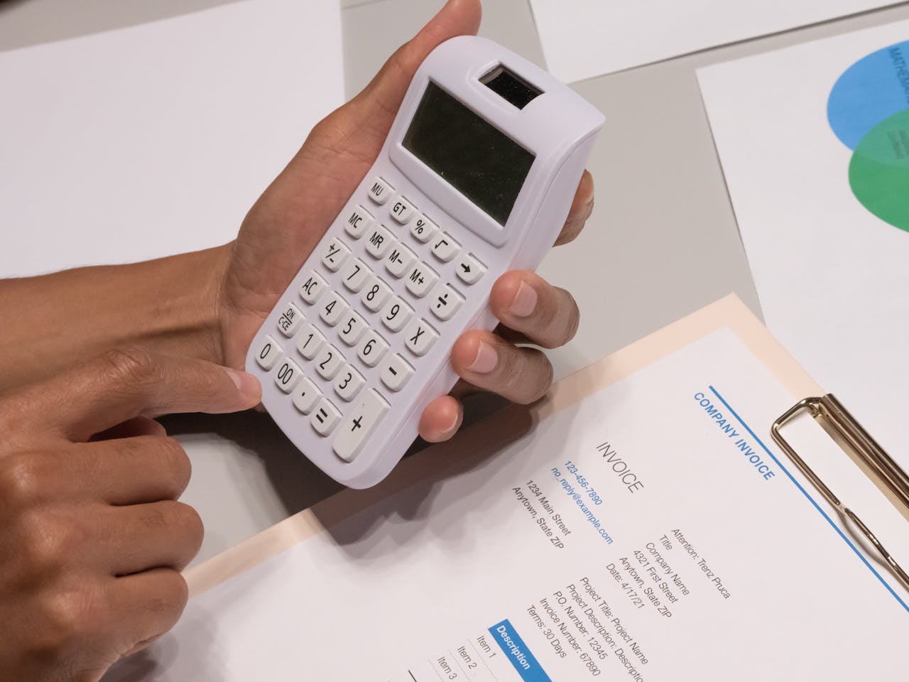 Close-up of hands using a calculator next to a company invoice, depicting a financial calculation concept.